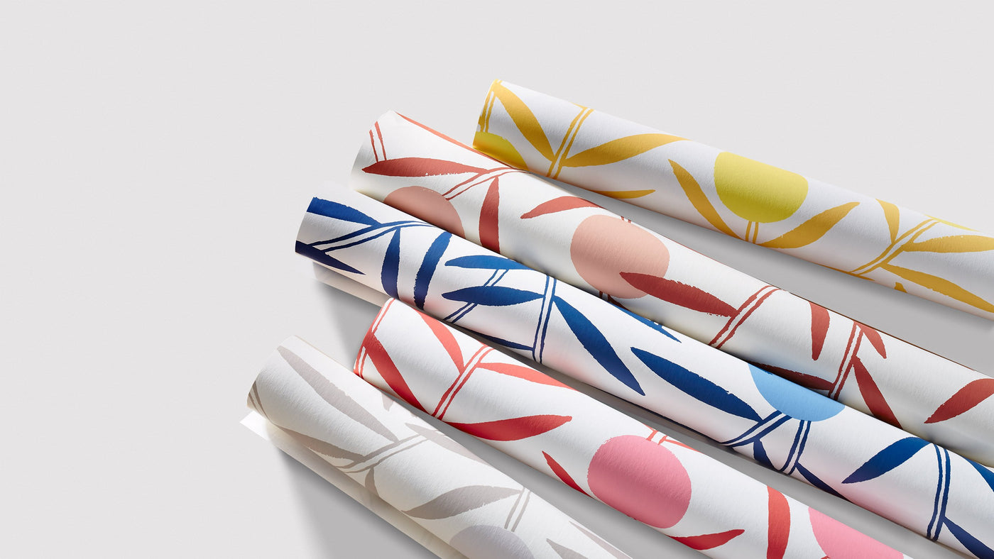 Five rolls of floral wallpaper, each in a different color, resting on a white background 